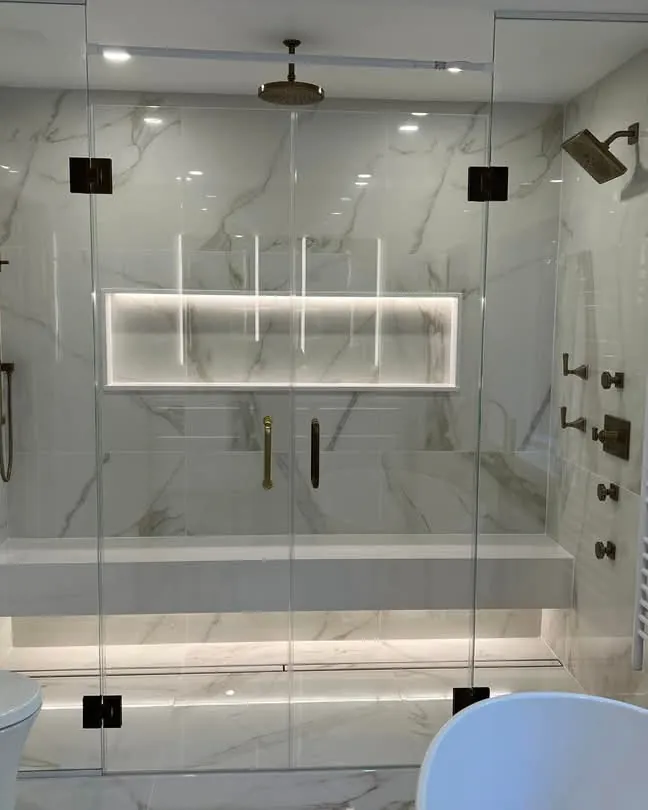 Marble tile walk-in shower with multiple shower heads, a backlit niche and frameless glass