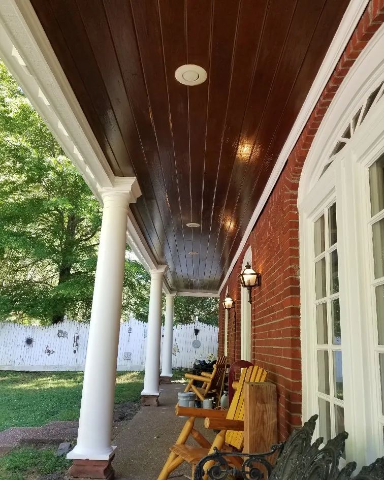 Covered front porch addition with white columns and a stained tongue-and-groove ceiling