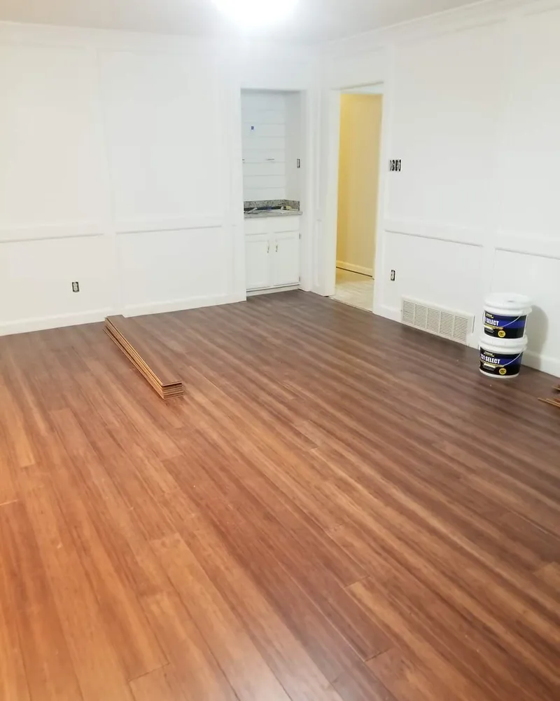Plank flooring installation in progress in an empty room with wainscot