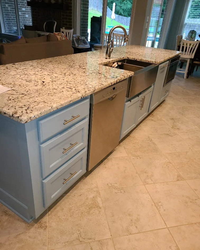 Kitchen with a stainless farmhouse apron sink, granite counters, blue base cabinets and travertine tile flooring