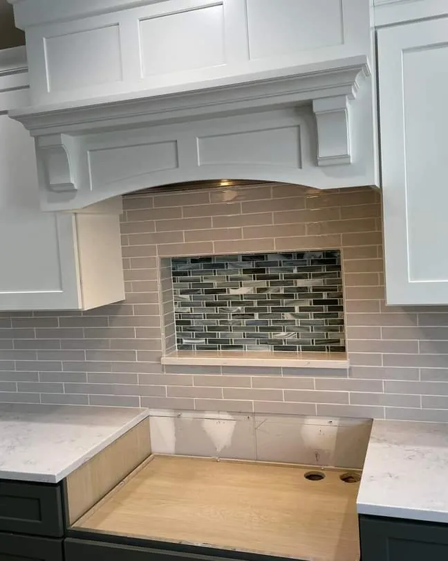 White kitchen with a custom wood vent hood, subway tile backsplash and a glass mosaic accent band