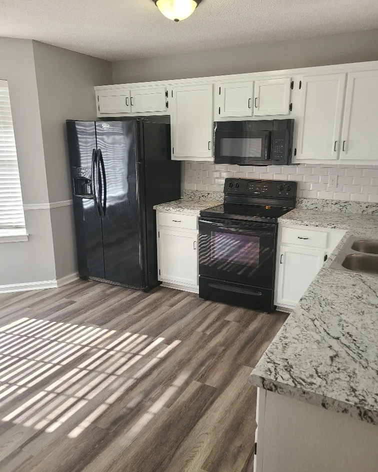 Kitchen with white cabinets, granite counters and new plank flooring after a wall was opened up
