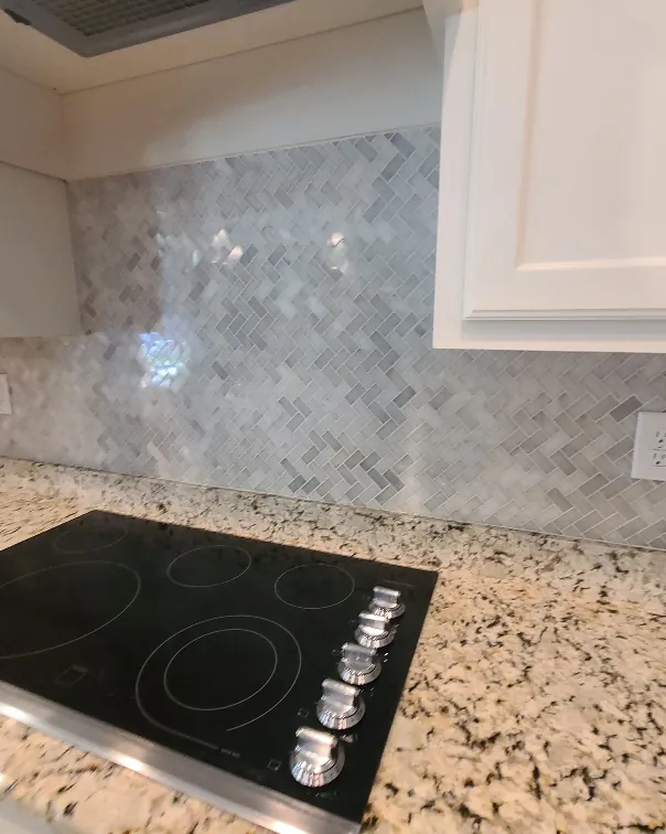 Cooktop set into granite counters with a marble tile backsplash and white cabinetry