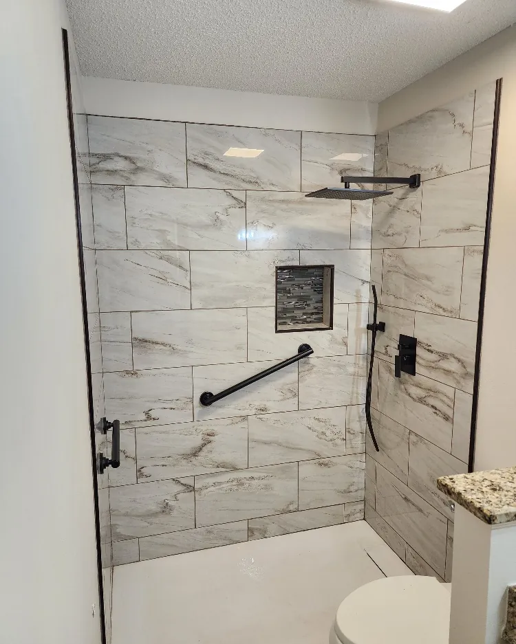 Finished marble-look tile shower with a black framed glass enclosure, built-in niche and grab bar