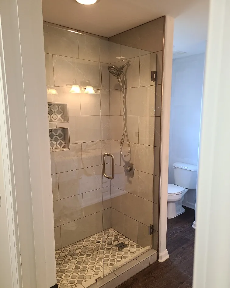 Walk-in glass shower with travertine tile walls, a built-in niche and a patterned tile shower floor