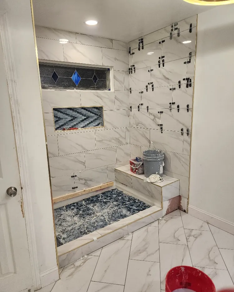 Marble tile shower under construction with a mosaic shower pan and a herringbone accent niche