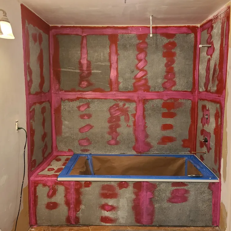 Red waterproofing membrane applied over a shower pan and walls before tiling