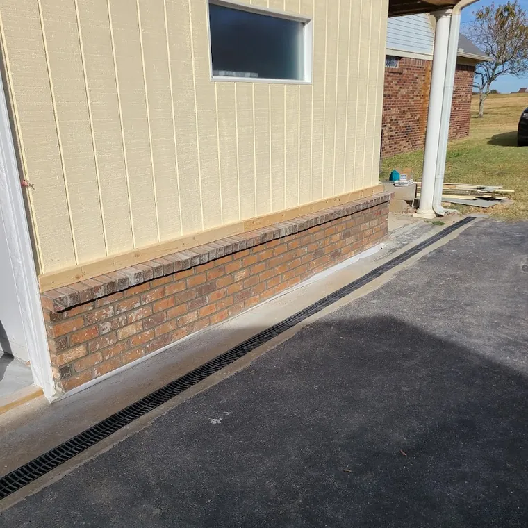 Exterior wall and driveway work in progress on a brick home