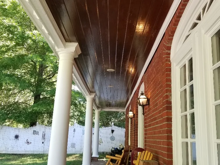 Covered front porch addition with white columns and a stained tongue-and-groove ceiling