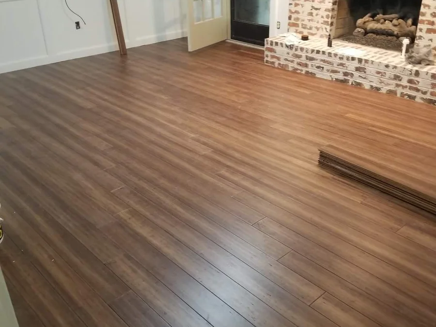 New wood flooring running through a living room with an exposed brick fireplace