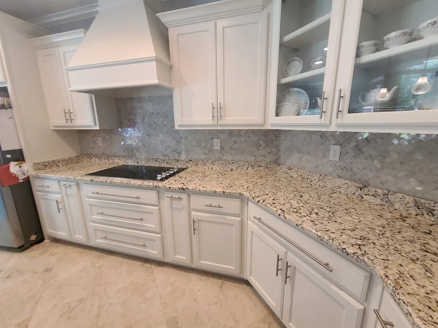 White kitchen remodel with a custom vent hood, granite counters and a marble tile backsplash